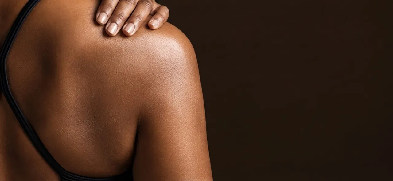 Mano sobre el hombro de una mujer, piel morena con luz cálida.